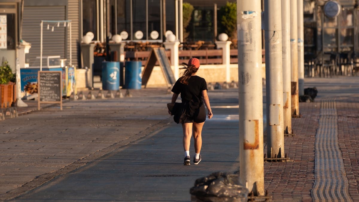 A woman enjoys a peaceful evening walk in Foça, İzmir, Türkiye. Urban street scene with warm sunset lighting.